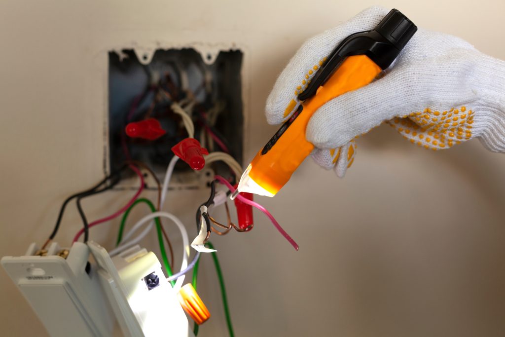 Electrician testing exposed wiring in a wall outlet